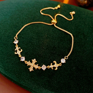 Détail d'un bracelet doré avec croix et fleur de lys orné de zircons blancs brillants