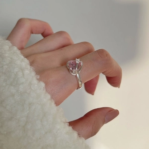 Close-up of a silver ring featuring a pink heart-shaped gemstone on a model's finger