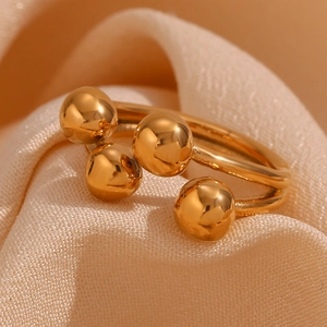 Close-up of a 18K gold plated open ring with four polished golden beads on silk fabric