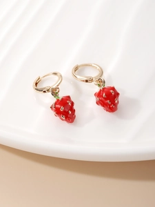 Macro detail of cute strawberry earrings with red enamel charms and gold hoops on a stand