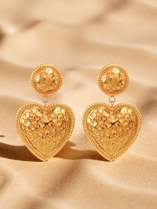 Detail of gold heart earrings with hammered metal texture on a soft sandy background