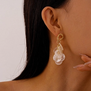 Close-up of model wearing gold textured hoop earrings with dangling shell discs