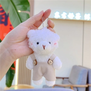 Detalle de llavero de osito de peluche blanco con peto beige y botones de madera