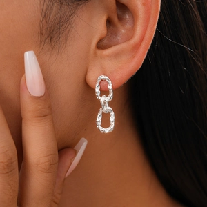 Gros plan de boucles d'oreilles chaînes argentées à texture martelée portées par un mannequin