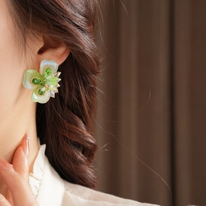 Gros plan de boucles d'oreilles florales avec gemmes vertes portées par un mannequin sur fond sombre