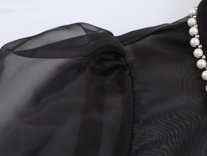 Detail of elegant black organza blouse featuring delicate pearl trim on the collar