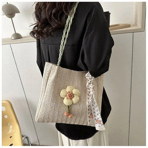 Detail of woven straw tote with green strap, yellow flower charm and silk scarf knot