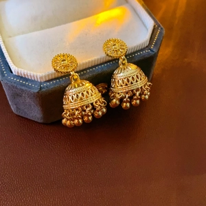 Macro detail of gold-plated Jhumka bell earrings with intricate tassels on velvet