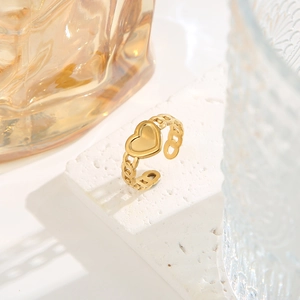 Elegant gold heart ring with chain design on white stone under bright sunlight