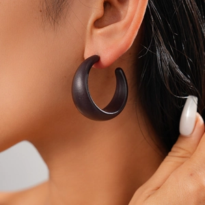 Close-up of a matte black acrylic C-shaped geometric hoop earring worn by a model