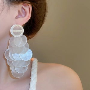 Close-up of layered white shell drop earrings worn by a model for a coastal look