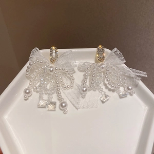 Macro view of lace bow earrings with pearl tassels and crystal beads on a display tray