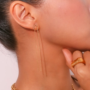 Macro shot of gold long tassel chain earrings and a wide irregular ring on a model