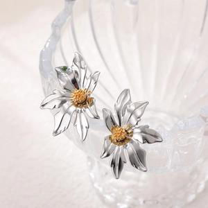 Close-up of silver flower earrings with gold center on textured glass edge