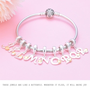 Detailed shot of S925 silver charm bracelet with gold heart letters J to R on pink background