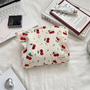 Détail de la trousse de voyage en seersucker à motif cerises sur lit blanc