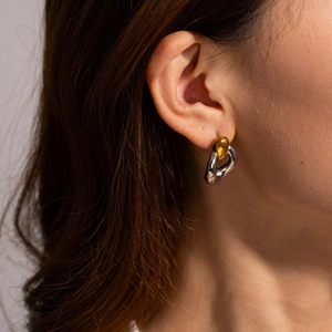 Gros plan de boucles d'oreilles bicolores dorées et argentées portées par un mannequin