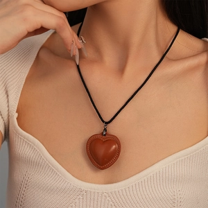 Detail of brown faux leather heart pendant on a black cord worn over a white knit sweater