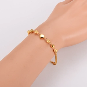 Polished gold stainless steel beaded bracelet with heart pendant on woman's wrist