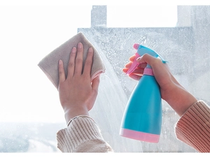 Action shot of blue and pink spray bottle and microfiber cloth cleaning a bright window