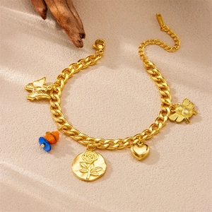 Détail du bracelet à breloques en acier doré avec pendentifs rose et cœur sur fond de sable