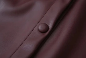 Makroaufnahme von Nähten und Knöpfen an einem burgunderroten PU-Leder-Set aus Rock und Jacke