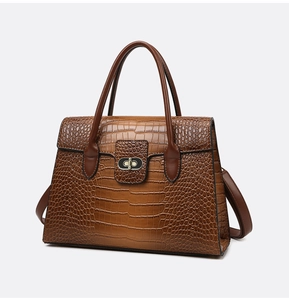 Detailed view of brown crocodile texture handbag with gold metal lock and leather handle