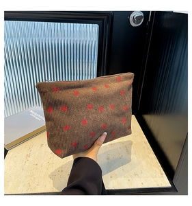 Detail of a brown corduroy clutch bag featuring a red strawberry print with zip closure