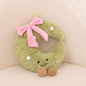 Detail showing green C-shaped plush toy with pink bow, pearls and cute smiling face