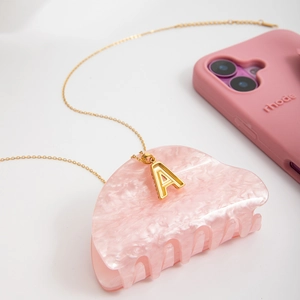 Close-up of gold letter A pendant necklace displayed on pink marble accessory