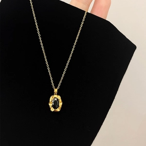 Vintage gold necklace with oval black gemstone pendant on a dark textile background