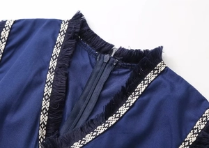 Détail du col en V d'une robe bleu marine avec bordure à franges et fermeture invisible