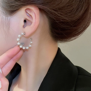 Close-up of elegant C-shaped pearl earrings with silver twisted metal design on model