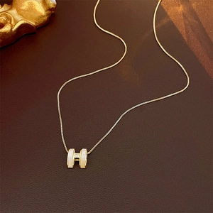 Golden H-shaped pendant necklace with zircon accents on dark leather background