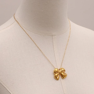 Close-up of a gold bow pendant necklace on a beige display stand for a luxury look
