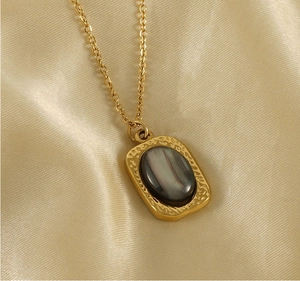 Macro detail of gold titanium necklace featuring a square tiger eye stone pendant on silk