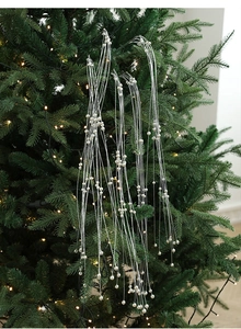 Détail de la chaîne de perles argentées suspendue sur un sapin de Noël avec lumières chaudes