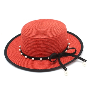 Detail of red straw boater hat with black ribbon, white pearls and side bow accent