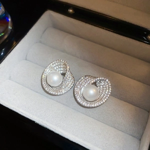 Detailed view of silver wave earrings with sparkling stones and centered white pearls