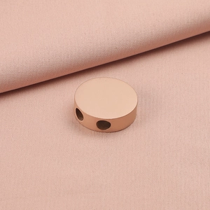 Macro detail of rose gold stainless steel round bead with double holes on pink fabric