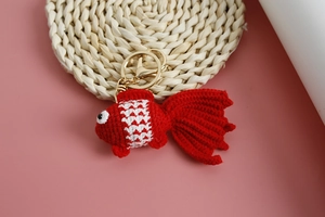 Close-up of handmade red and white crochet goldfish keychain on a woven coaster