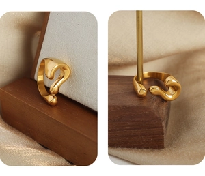Detail view of gold-plated titanium question mark ring on a wooden display stand