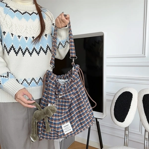 Blue and orange plaid drawstring bucket bag detail with a plush charm on a model