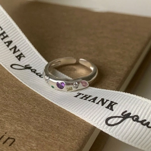 Detailed shot of open silver ring with colorful zircon hearts on gift packaging