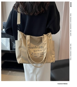 Detail of beige canvas tote bag showing side pocket, wide strap and printed lettering