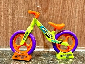 Macro shot of green and orange toy balancing bike with purple tires on wood background