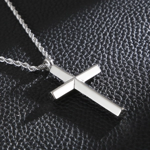 Macro view of silver cross pendant with twist chain on black leather background