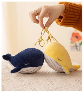 Detail of plush whale keychains in blue and yellow with gold metal rings held by hand