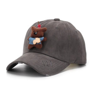 Detailed shot of a brown plush bear and cherry charm on a distressed baseball cap