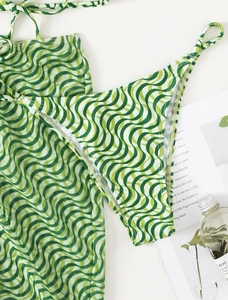 Flat lay of green and white wave pattern bikini set with matching sarong and accessories